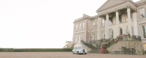 Grand estate featuring elegant architecture, lush greenery, and a classic car at the entrance, perfect for a romantic wedding backdrop.