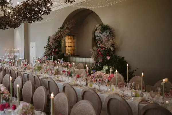 Elegant reception setup featuring a long table adorned with floral arrangements, candles, and subtle greenery, perfect for a romantic wedding.