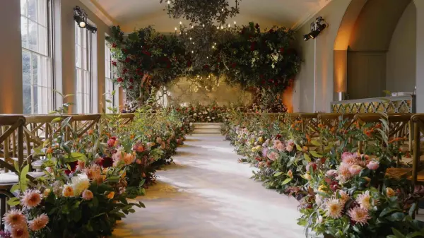 Lush floral arrangements line a romantic aisle leading to an enchanting altar adorned with greenery and soft lighting in an elegant venue.