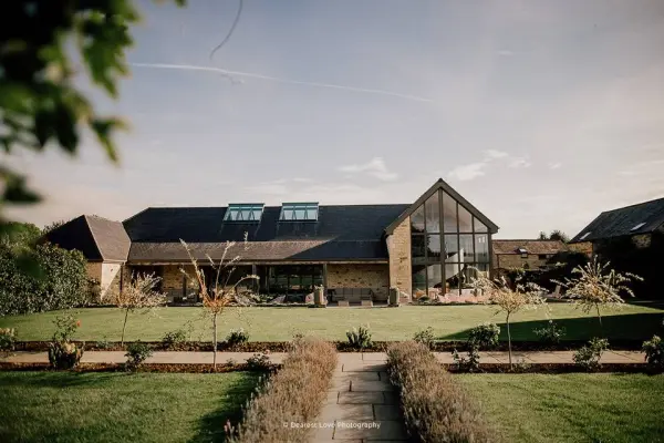 Stunning countryside venue with a modern glass facade, surrounded by lush gardens and a charming stone pathway. Perfect for outdoor ceremonies.