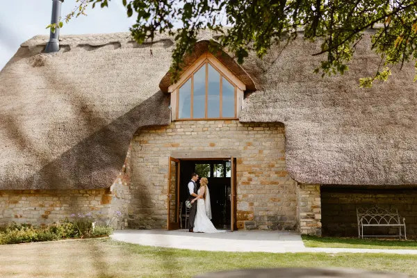 Charming thatched barn entrance framed by lush greenery, perfect for romantic outdoor ceremonies or intimate receptions.