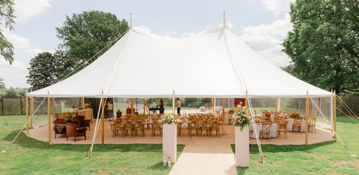 Elegant outdoor tent venue with wooden tables, surrounded by greenery, perfect for a stylish wedding celebration.