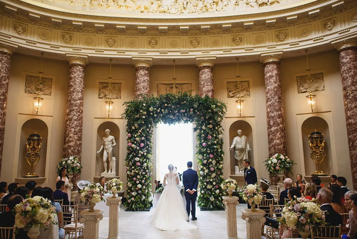 A stunning indoor ceremony space featuring marble columns, floral archway, and elegant seating, creating a romantic atmosphere for vows.