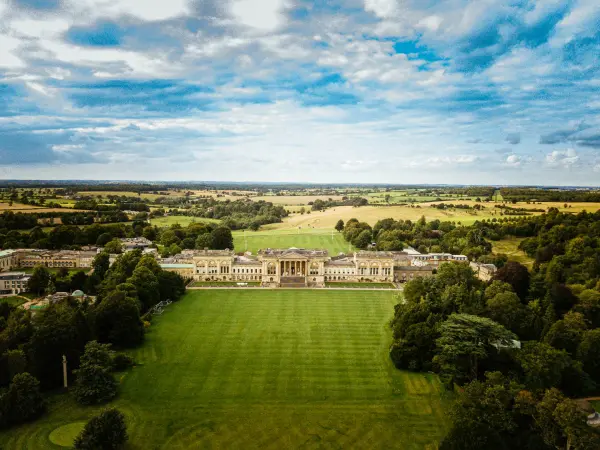 Stunning aerial view of a grand estate surrounded by lush green fields and mature trees, ideal for outdoor ceremonies and elegant receptions.