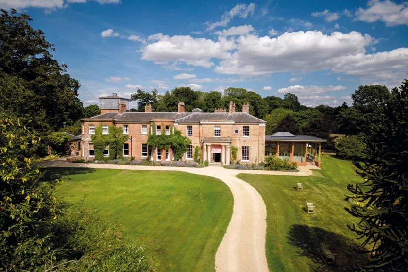 Elegantly restored mansion surrounded by lush greenery, featuring a winding driveway and classic architectural details, perfect for outdoor ceremonies.