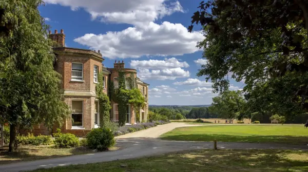 Stunning historic estate featuring spacious lawns, manicured gardens, and a charming brick façade under a blue sky with fluffy clouds.