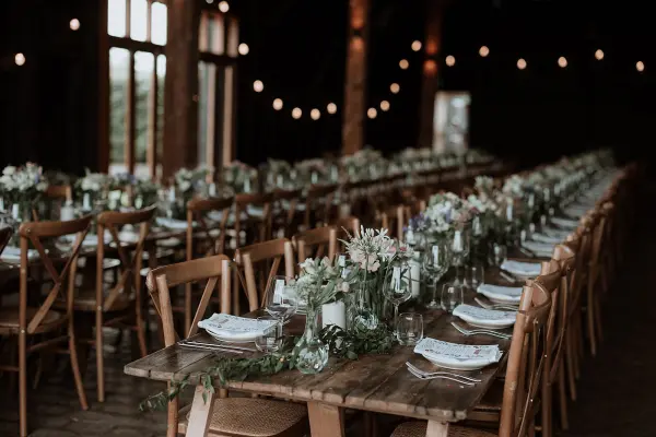 Charming rustic venue with long wooden tables adorned with elegant centerpieces and soft lighting creating a warm, inviting atmosphere.
