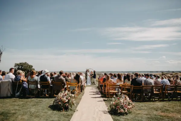 Charming outdoor wedding ceremony with guests seated on lush grass, a floral aisle leading to a beautiful skyline backdrop.