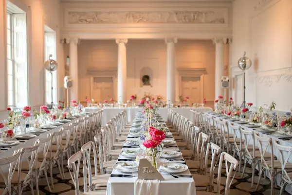 Bright banquet room featuring elegant white tables adorned with floral centerpieces, tall columns, and soft lighting for a romantic atmosphere.
