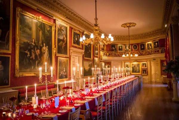 Elegant reception hall adorned with historic paintings, featuring a long red table set with candles and fine china, creating a romantic atmosphere.