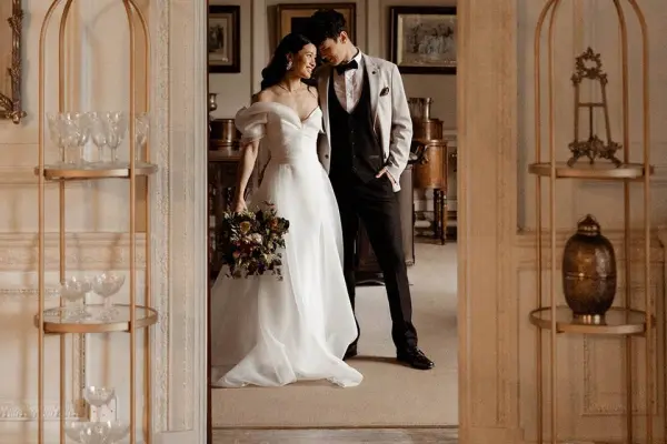 A couple in elegant attire shares a tender moment in a sophisticated venue with vintage decor and warm, inviting ambiance.