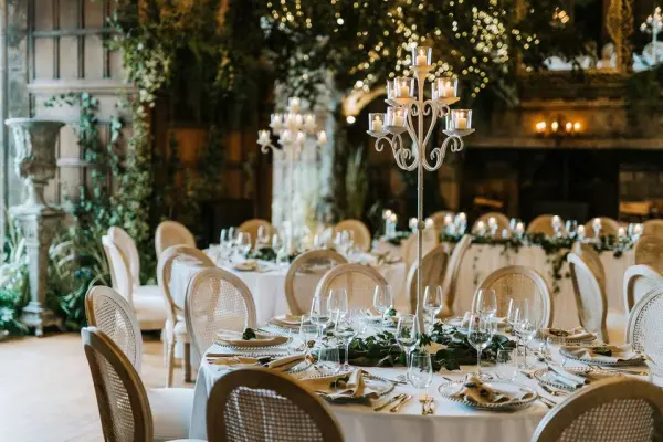 Elegant tables set with fine china and crystal glasses, surrounded by lush greenery and soft candlelight in a beautifully decorated reception hall.