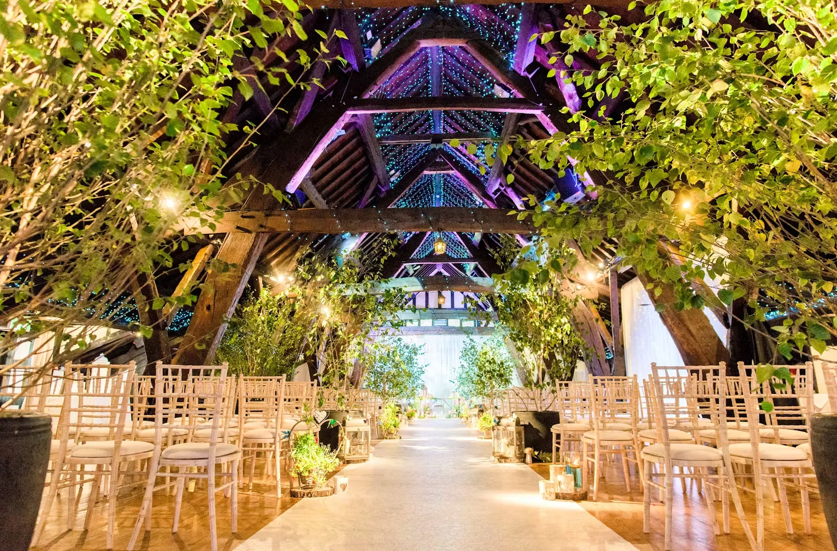 Charming rustic barn with exposed beams, decorated with greenery, and an inviting aisle lined with elegant chairs for a romantic ceremony.