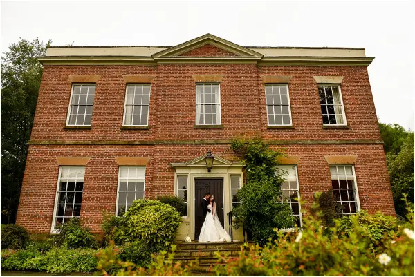 Charming brick mansion surrounded by lush greenery, featuring a grand entrance perfect for wedding ceremonies and photos.