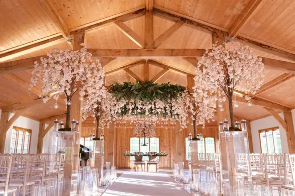 Rustic wooden interior with elegant floral arrangements, clear acrylic chairs, and a stunning greenery backdrop for intimate ceremonies.