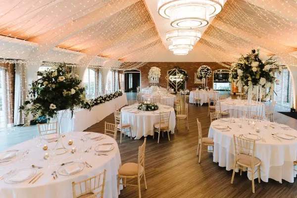 Elegant reception space featuring round tables adorned with floral centerpieces, draped ceilings, and soft lighting accents for a romantic ambiance.