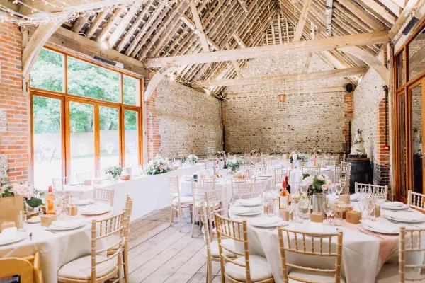 Rustic barn wedding venue featuring elegant round tables, wooden beams, and large windows that illuminate the space with natural light.