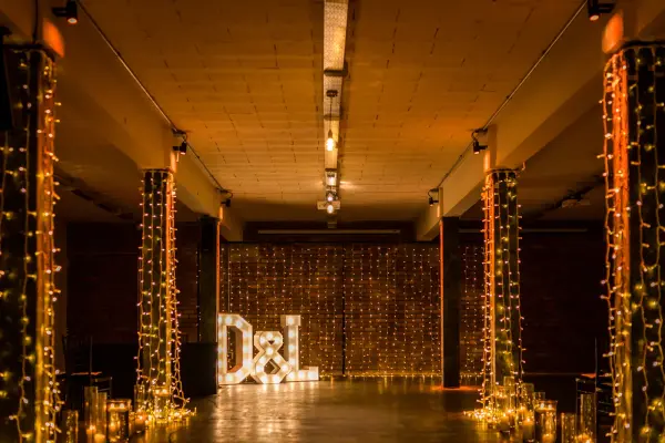 Twinkling fairy lights drape elegantly from columns, illuminating a stylish event space featuring a personalized monogram display.