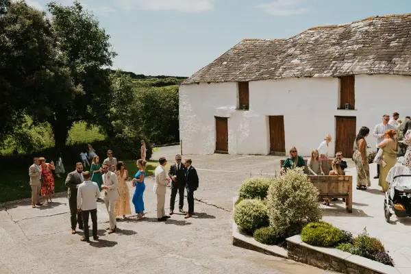 Charming outdoor gathering near a rustic white barn, surrounded by lush greenery, perfect for a picturesque wedding celebration.