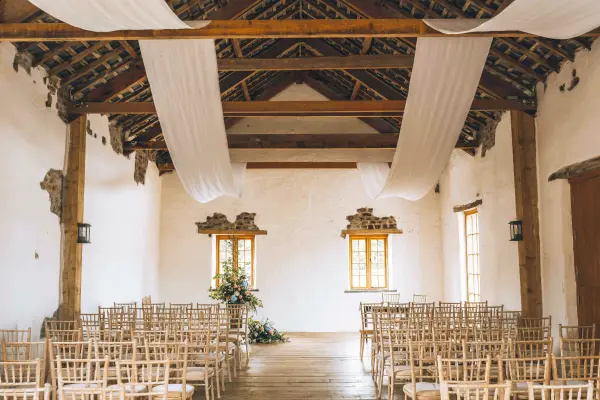 Rustic wedding ceremony space featuring wooden beams, elegant drapery, and natural light, surrounded by charming wooden chairs.