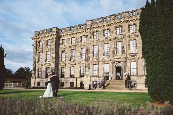 A stunning historic mansion serves as a backdrop for an outdoor wedding, featuring lush green lawns and elegant architecture.