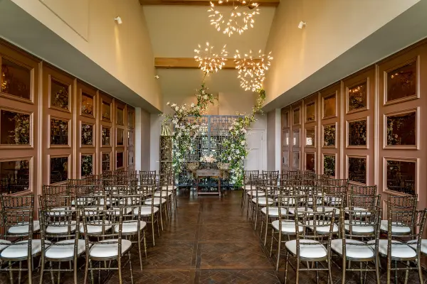 Stylish ceremony space featuring elegant chairs, lush greenery, and modern chandeliers, perfect for intimate wedding gatherings.