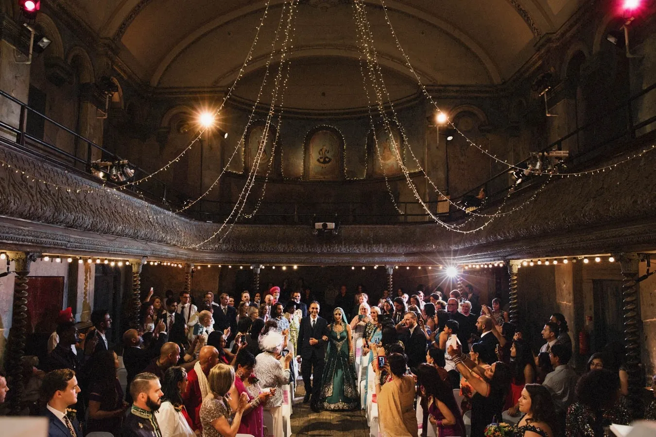 A stunning ceremony in an ornate, vintage venue with elaborate architecture and warm lighting, surrounded by guests celebrating the couple.