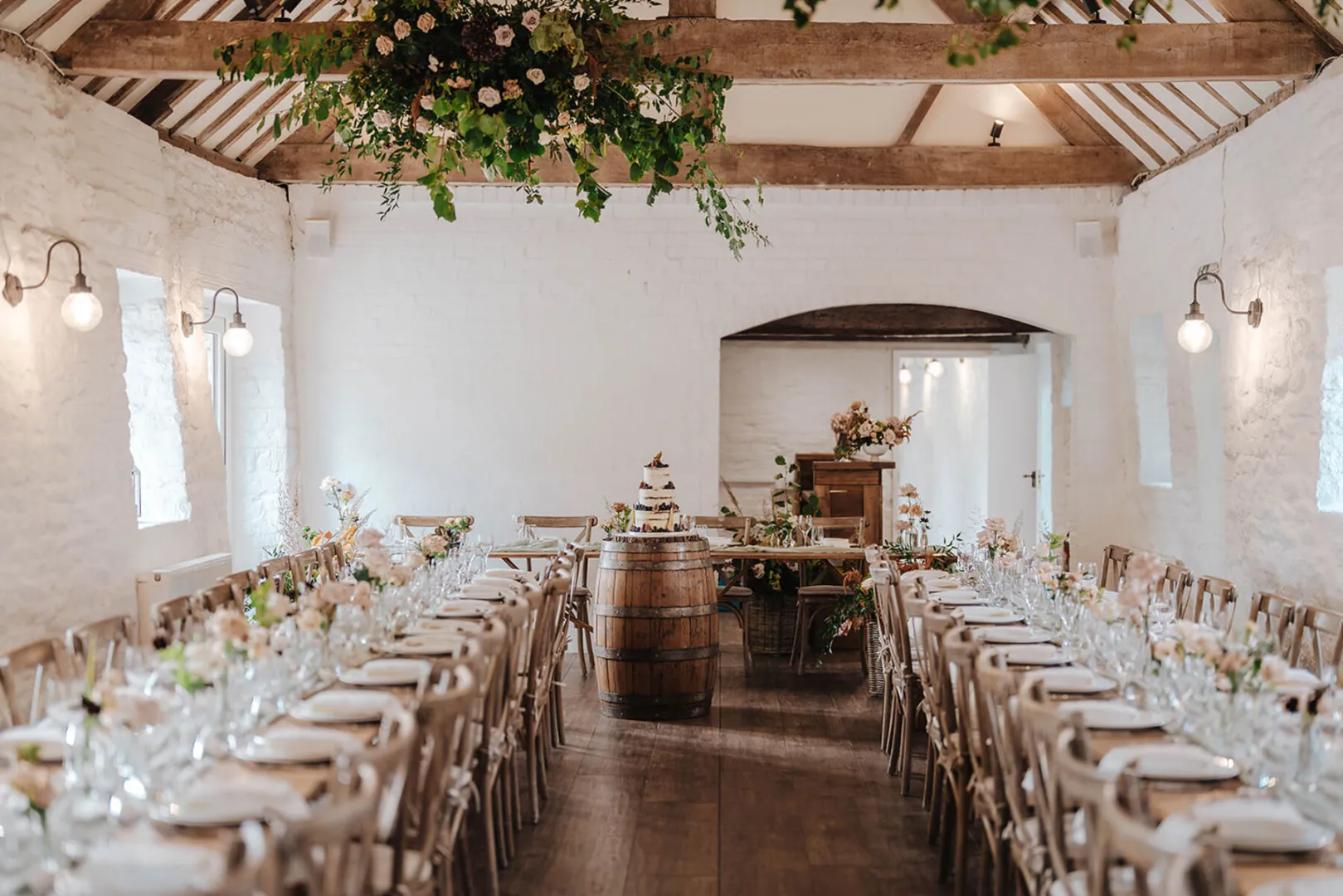 Charming rustic barn interior featuring wooden beams, elegantly set dining tables, and vibrant floral arrangements for a romantic wedding.