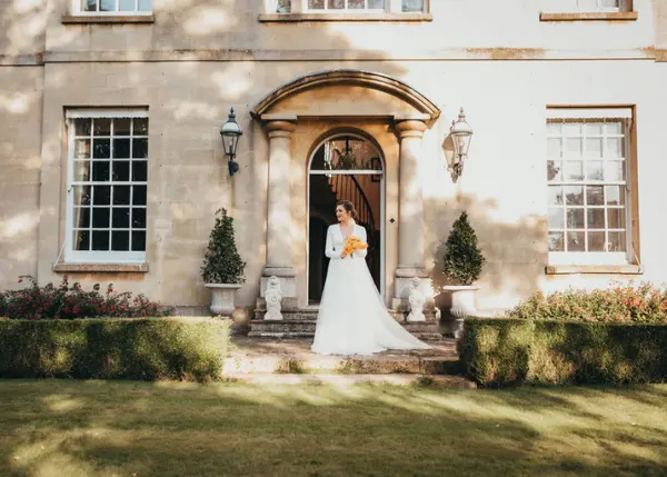 Elegant bridal portrait at a stately home entrance, featuring classic architecture, manicured lawns, and charming garden details.