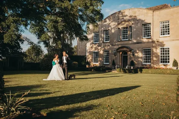 Couple stands amidst lush greenery, framed by a grand historic building, ideal for romantic outdoor ceremonies and elegant photo opportunities.