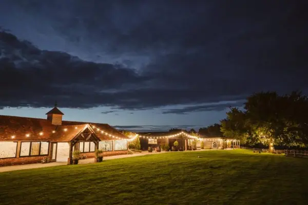 A charming venue at dusk, featuring a sprawling lawn, warm string lights, and rustic architecture, perfect for outdoor celebrations.