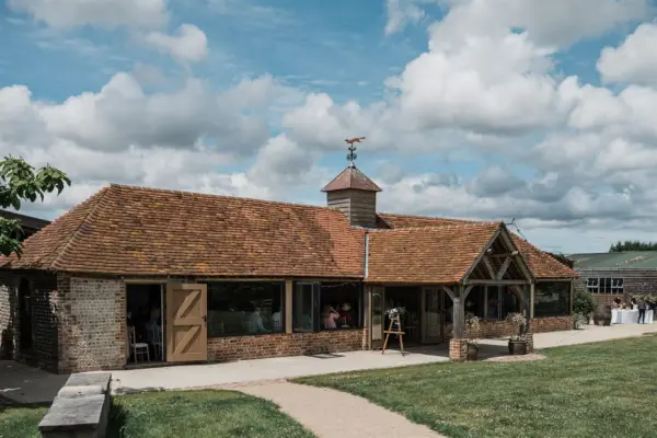 Charming rustic barn venue with a thatched roof, large windows, and lush green surroundings, perfect for elegant weddings and celebrations.