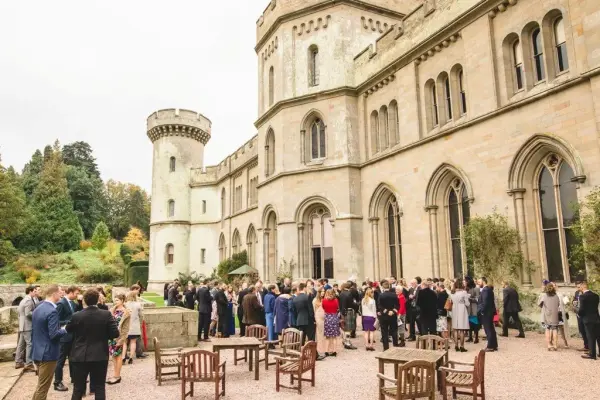 Guests mingling in a charming courtyard by a historic castle with elegant architecture and lush greenery, perfect for a romantic wedding.