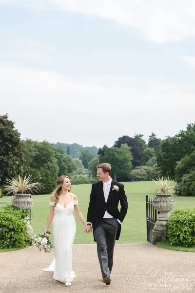 A couple strolls hand-in-hand down a scenic path, featuring lush greenery and elegant landscaping, ideal for outdoor wedding ceremonies.