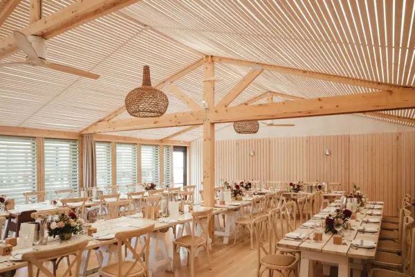 Spacious reception area featuring wooden beams, elegant tables set with floral arrangements, and natural light streaming through large windows.