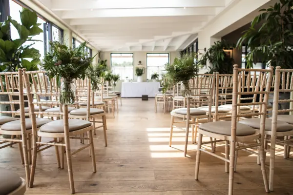 Light-filled ceremony space with elegant chiavari chairs and greenery accents, creating a fresh, inviting atmosphere for weddings.