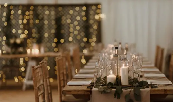 Rustic wooden tables elegantly set with candles and greenery, surrounded by twinkling fairy lights for a romantic wedding atmosphere.