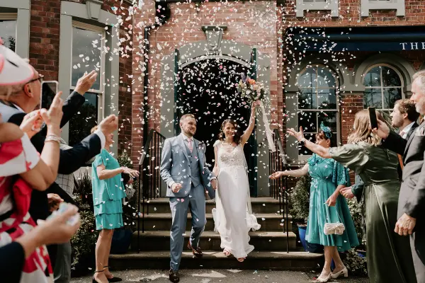 Newlyweds rejoice, showered with confetti on steps, surrounded by cheerful guests in vibrant attire, celebrating a joyful outdoor ceremony.