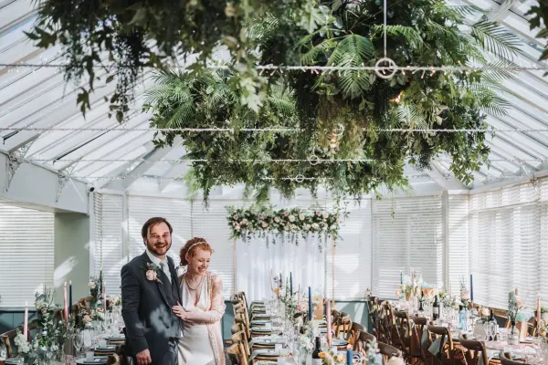 A charming greenhouse venue featuring greenery, long wooden tables, and intimate lighting, perfect for a romantic wedding celebration.