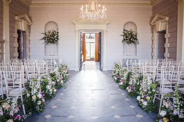 Elegant indoor ceremony space featuring white chiavari chairs, floral arrangements, and a chandelier, creating a romantic ambiance.