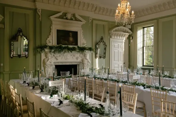 Elegant reception space with gold accents, a fireplace, lush greenery, and long tables set for a wedding celebration.