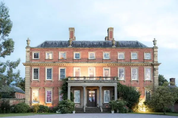 Elegant brick manor with grand entrance, tall windows, and lush landscaping, perfect for a romantic wedding celebration.