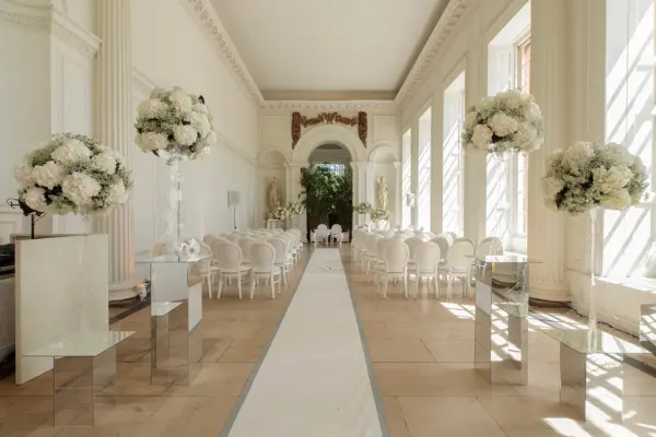 Elegant ceremony space with tall floral arrangements, white chiavari chairs, and a charming aisle, bathed in natural light.