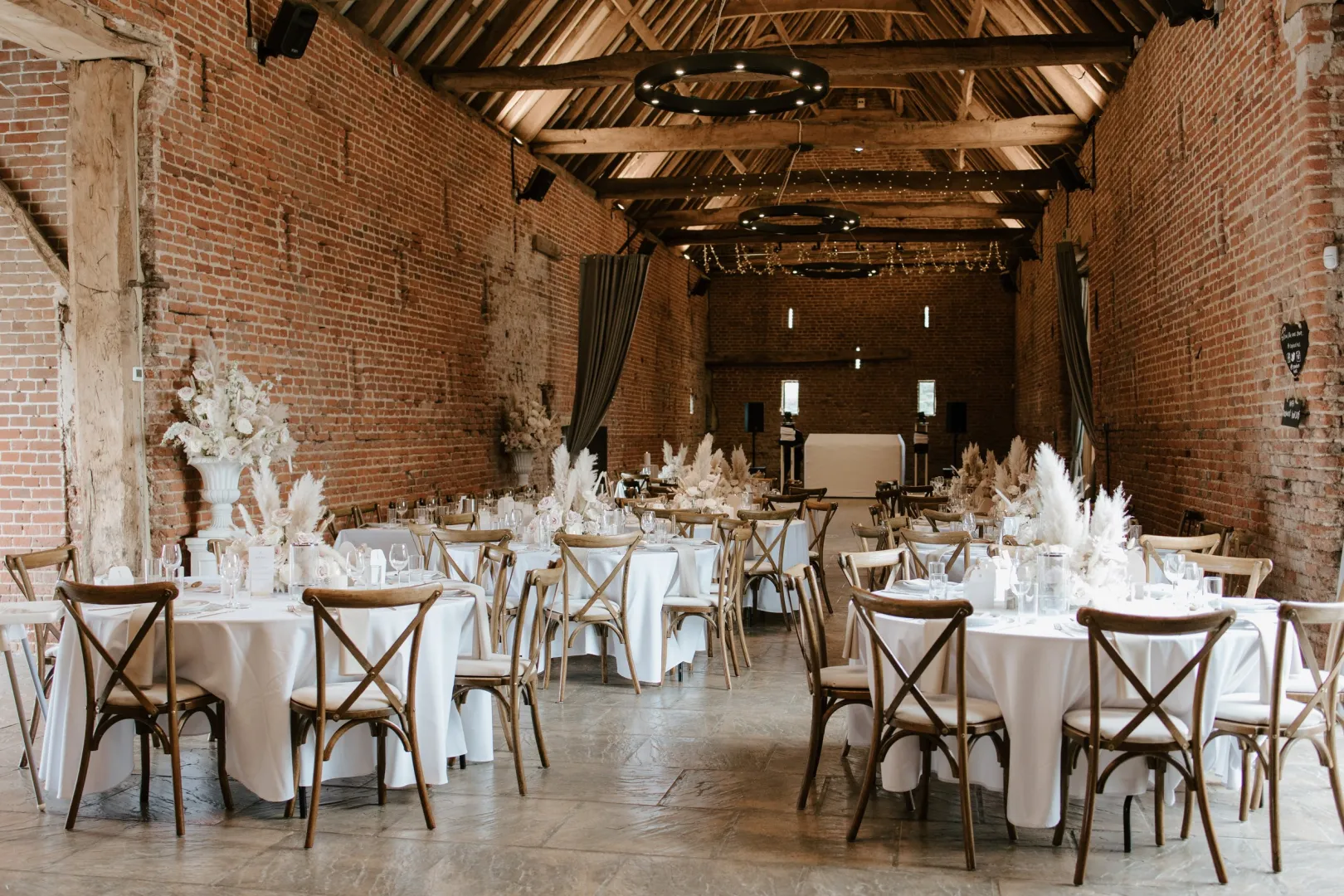 Elegant barn venue featuring rustic exposed brick, wooden beams, and beautifully adorned tables set for a wedding reception.