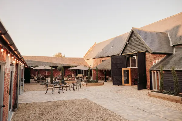 Charming rustic barn venue features a spacious outdoor courtyard with patio seating, umbrellas, and warm string lights for an inviting atmosphere.
