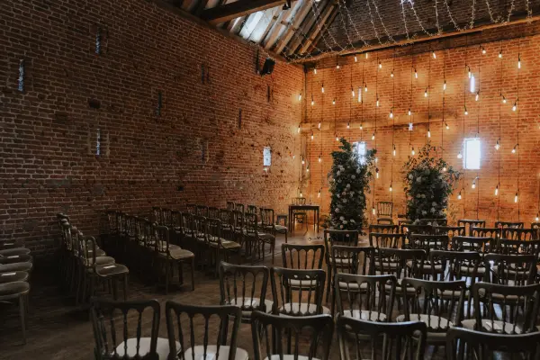 Rustic ceremony space with exposed brick walls, wooden chairs, and ambient string lights creating a cozy, romantic atmosphere.