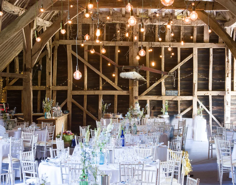 Rustic barn interior featuring elegant tables, vintage chandeliers, and twinkling string lights, perfect for a charming wedding reception.