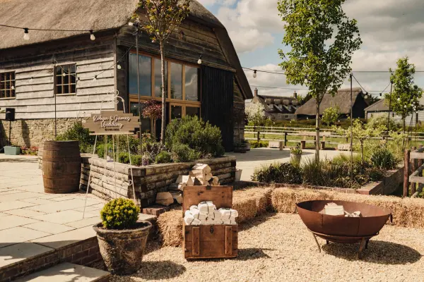 Charming rustic barn venue surrounded by lush greenery, featuring a cozy outdoor space with hay bales and decorative planters.