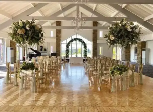 Elegant indoor wedding venue with towering floral arrangements, a spacious layout, and large windows creating a bright, inviting atmosphere.