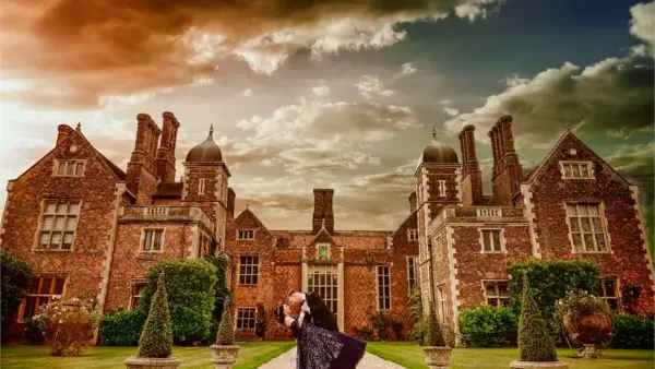 Charming historic mansion with intricate brickwork, lush gardens, and dramatic sky, perfect for romantic wedding portraits.